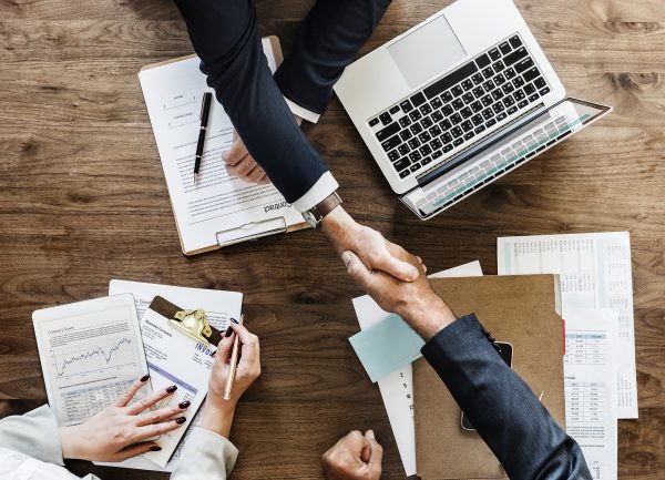 business people shaking hands over a table with computers